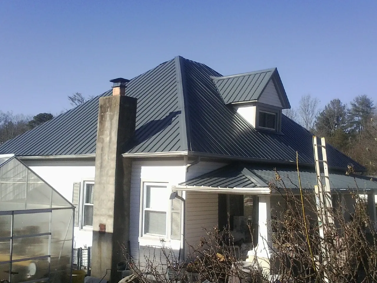 Dark blue standing seam metal roof on a white farmhouse with dormer — Slate & Tile Roof Repair by Roofing Brothers in El Dorado Springs