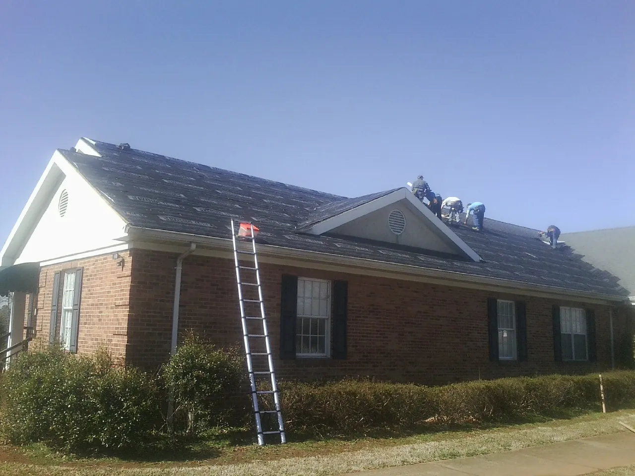 Crew tearing shingles off a brick ranch roof with a ladder set — Metal Roof Repair work by our crew in El Dorado Springs