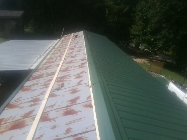 Old rusted panels beside newly installed green metal roofing — Wind Damage Roof Repair by Roofing Brothers in El Dorado Springs
