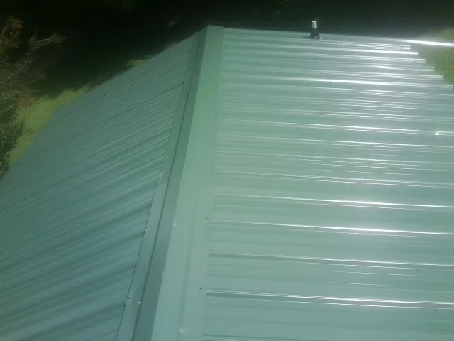 New green metal panels meeting at the ridge of a roof — Flat Roof Repair work by our crew in El Dorado Springs