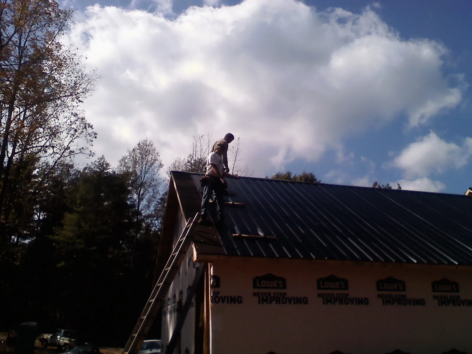 Roofer fastening dark metal panels high against a cloudy sky, from a Roof Inspection job in El Dorado Springs