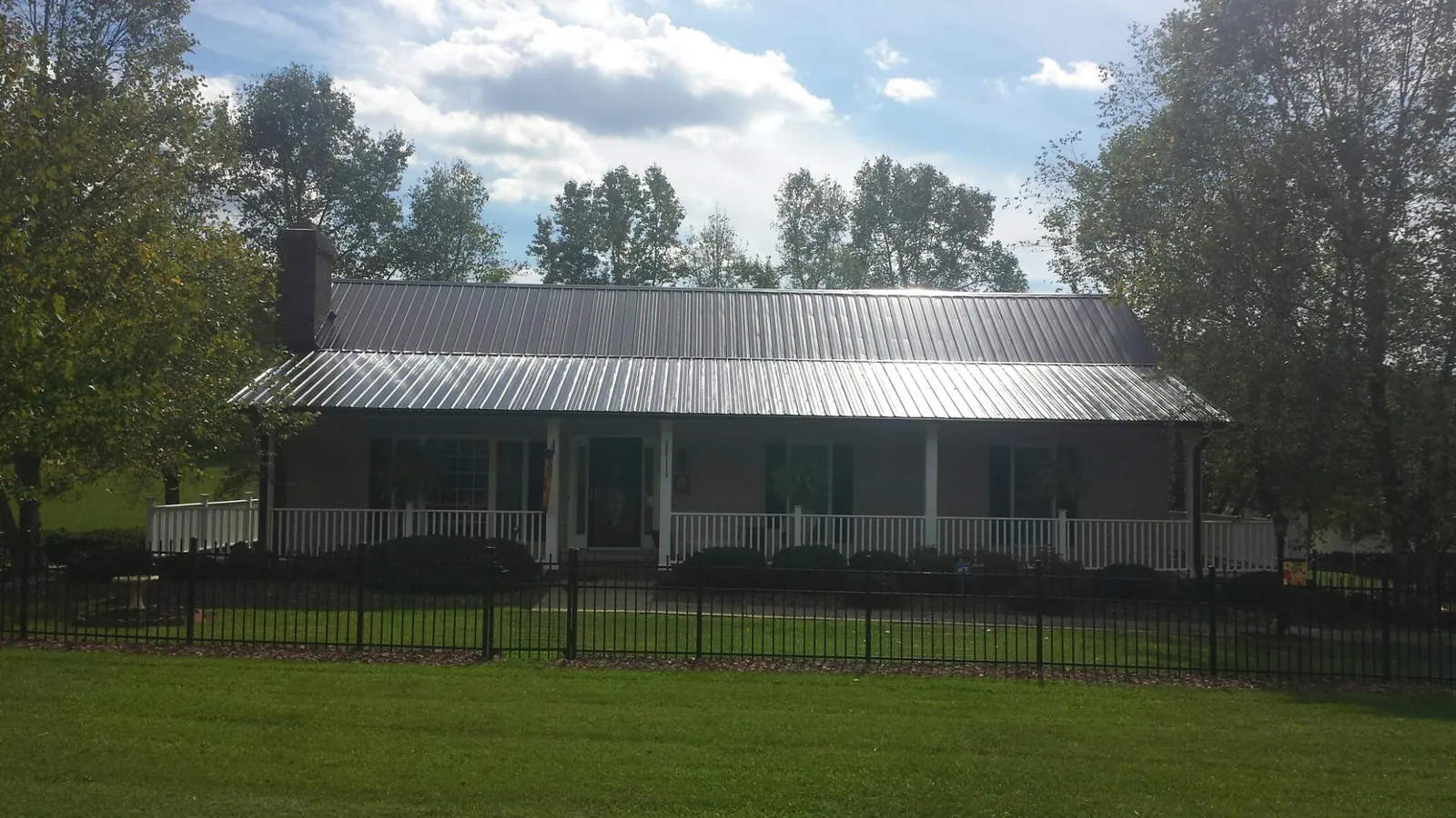 Gray metal roof on a brick ranch with a full width front porch — Gutter Guard Installation work by our crew in El Dorado Springs