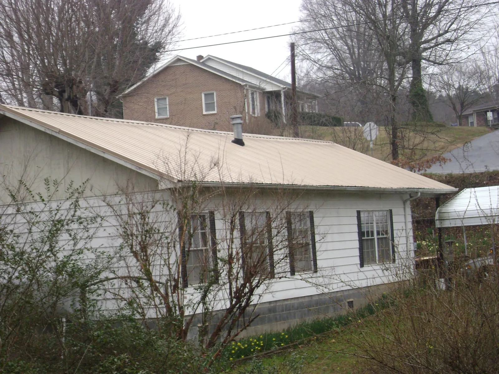 Tan metal roof on a white sided house set into a hillside — Commercial Roofing by Roofing Brothers in El Dorado Springs