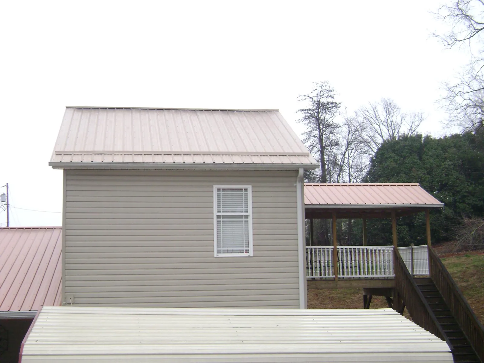 Tan metal roofs on a two story addition and attached porch, from a Roof Replacement job in El Dorado Springs